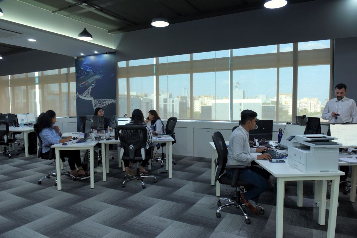 Team van professionals werkt in een modern kantoor met uitzicht op een stedelijke skyline, symbool voor productiviteit en technologische vooruitgang.